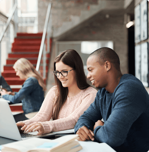 Um homem negro observando uma mulher branca de óculos digitando em um notebook,com uma mulher loira e uma escada com degraus vermelhos ao fundo.